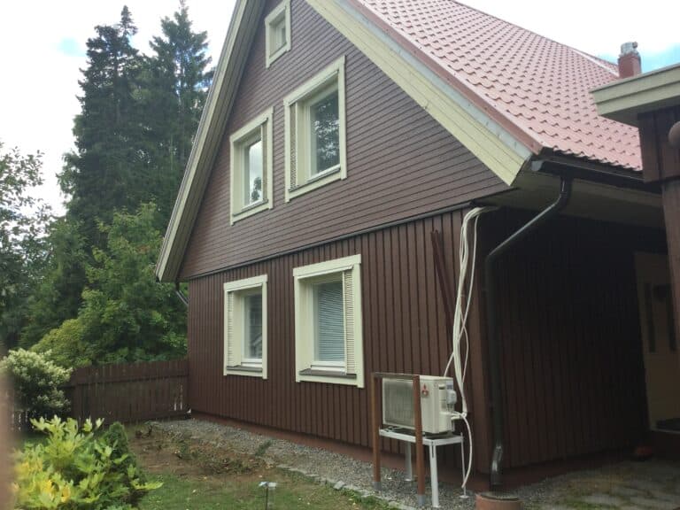 Puutalon ruskea pystylaudoitus, vaaleat ikkunanpielet ja nurkkalaudat.