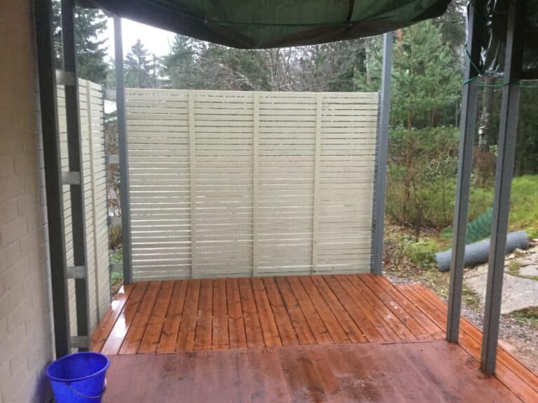 Vaalea vaakarimainen näkösuojaseinä ruskealla terassilla.