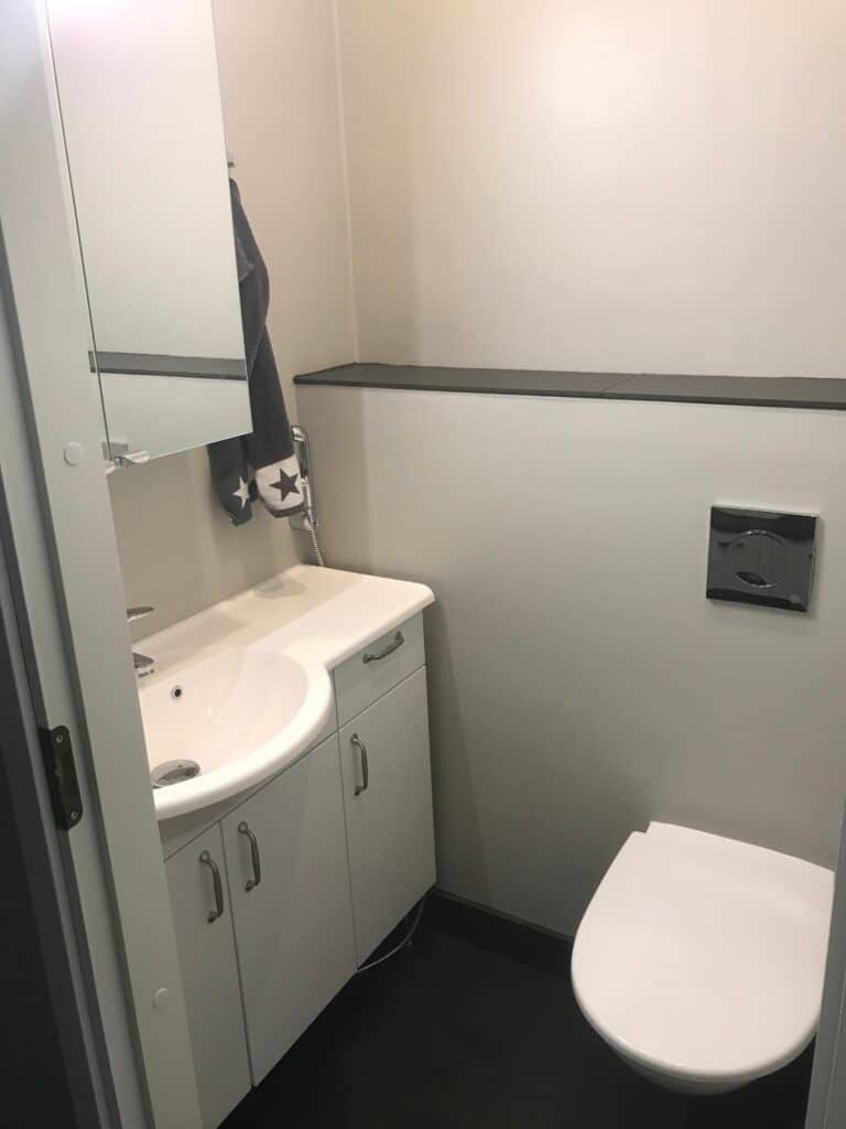 WC-tila, valkoinen allaskaappi ja tummalla raidalla jaettu seinä.