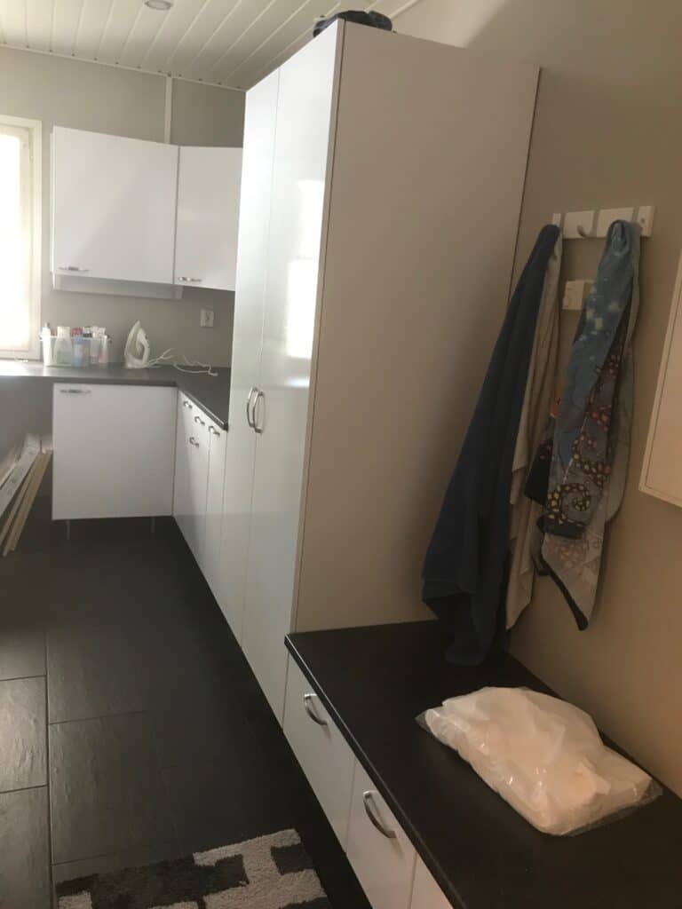 Korkea valkoinen säilytyskaappi kylpyhuoneessa pesutilan vieressä.