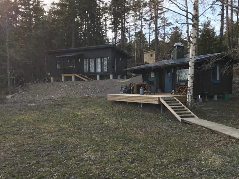 Piharakennuksia, laaja puuterassi ja pihaan laskeutuvat puuportaat.