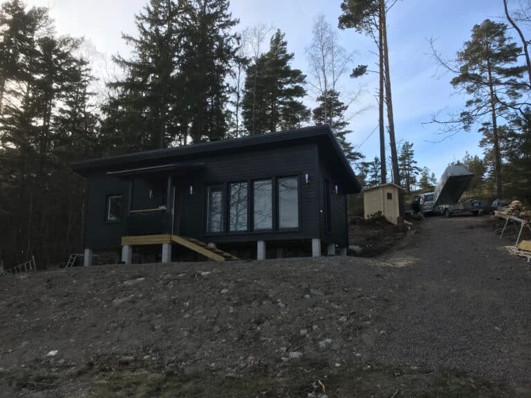 Tumma piharakennus metsäisessä ympäristössä ja keskeneräinen kulkureitti.