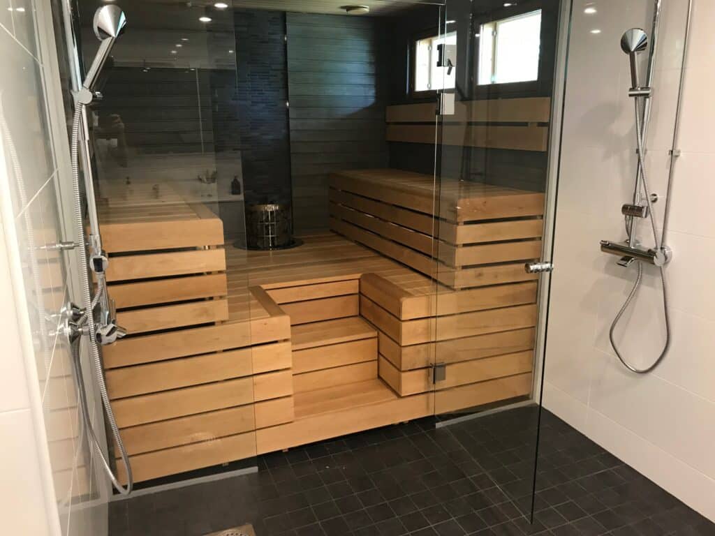 Kylpyhuoneen suihkutila ja lasiseinäinen sauna puulauteineen