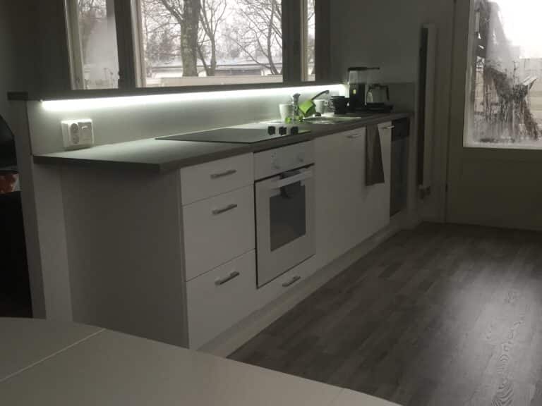 Valkoiset keittiökaapistot, tumma työtaso ja leveä ikkuna altaan yläpuolella.