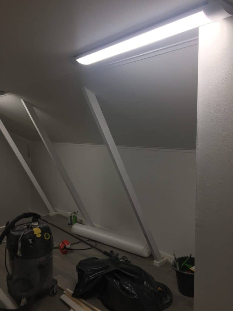 Vinokattoinen tila sisätöiden aikana, seinällä työvalo ja lattialla työkaluja.